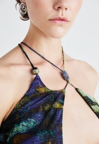 Violeta un zaļš rakstains audums halter tops ar spageti siksnām, kas rotāta ar dekoratīvām pērlēm nostiepuma dizainā gar apkakli.