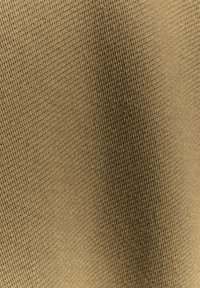 Nahaufnahme eines hellbraunen gewebten Stoffes mit strukturiertem Strickmuster und subtilen Schattierungen durch Stofffalten.