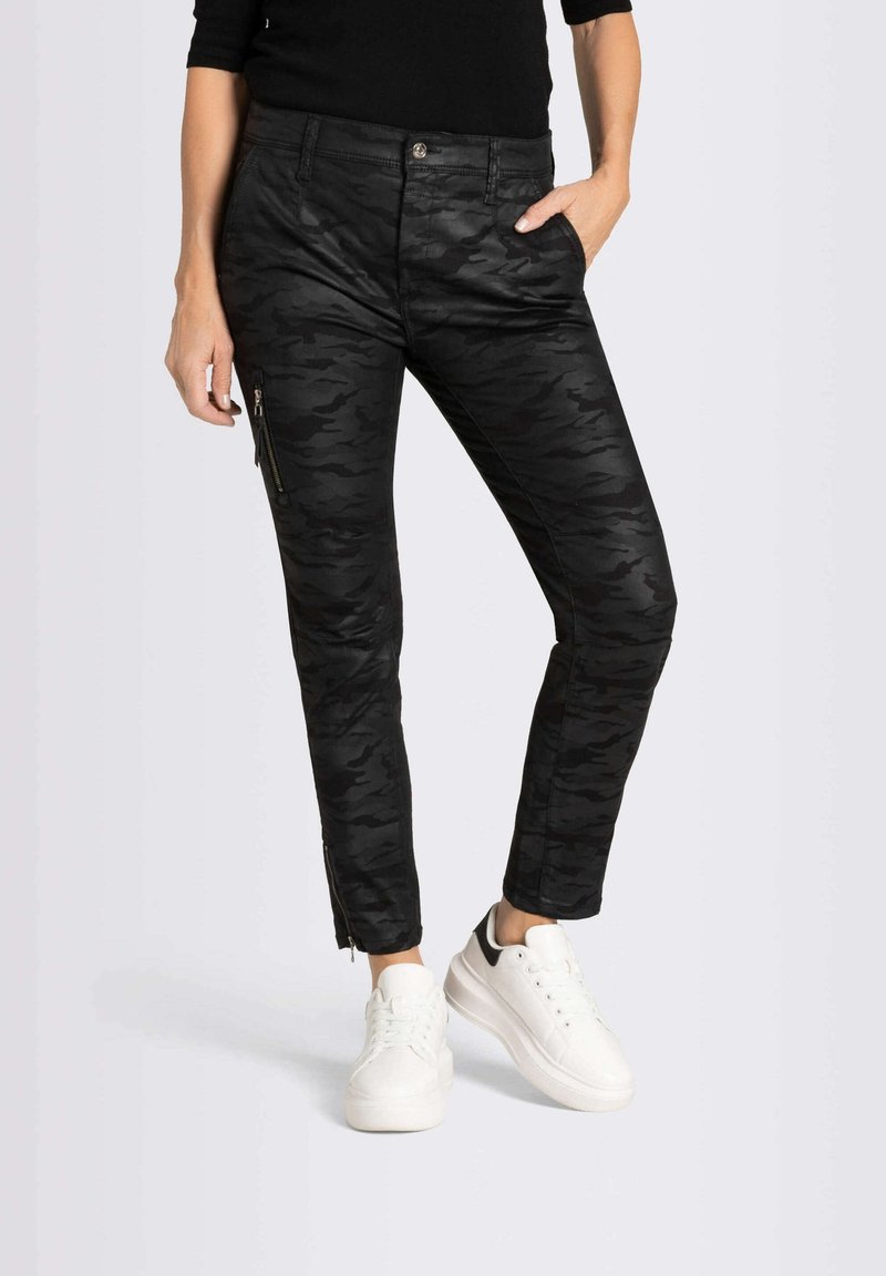 Pantalones de camuflaje negro con corte ajustado, cremalleras en los puños de los tobillos y bolsillos delanteros, combinados con zapatillas blancas.