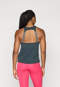 Donkergrijze sporttanktop met open rug en gebrandmerkte bandjes, aangevuld met felroze leggings. Gladde stof, fitted ontwerp.