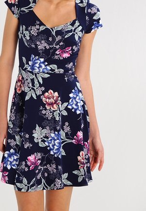 Sukienka w kwiaty na granatowym tle, z krótkimi rękawami i dopasowanym gorsetem. Wzór obejmuje różowe i niebieskie kwiaty z zielonymi liśćmi.