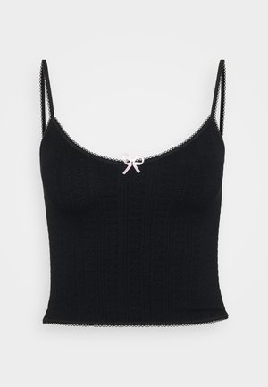 Black knitted camisole featuring thin straps, a scalloped hem, and a small pink satin bow at the center front. Textured pattern throughout.