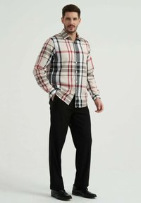Chemise à manches longues avec un motif à carreaux dans des tons de beige, noir, rouge et gris ; associée à un pantalon noir et des chaussures.