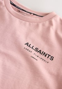 Hele roosa puuvillane t-särk, millel on ümar kaelus ja musta trükiga tekst "ALLSAINTS" ning "LONDON", allpool jaapani tähed.