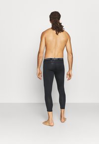 Czarne legginsy sportowe o dopasowanym kroju, z markowym paskiem w talii, wykonane z gładkiego, elastycznego materiału.