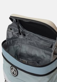 Insidan av en blå och grå ryggsäck visar slät tygfoder, dragkedjestängning och flera fickor. Svart kant längs den övre kanten.