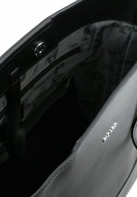 Zwarte leren handtasinterieur met een zilveren rits, logo-accenten en een grijze stoffen voering met een bedrukt patroon.