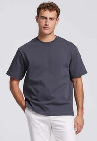 Antracietgrijze katoenen t-shirt met korte mouwen, ronde hals en een ontspannen pasvorm, gecombineerd met lichtgekleurde broeken. Geen zichtbare patronen of accenten.