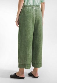 Zielone lniane spodnie o szerokich nogawkach z elastycznym pasem. Charakteryzują się skróconą długością i delikatną teksturą. Połączone z czarnymi wsuwanymi butami.