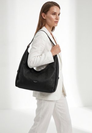 Donna con abito bianco che porta una grande borsa a tracolla nera strutturata con logo "Diana & Co Firenze" su sfondo neutro.