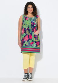 Kwiatowa tunika w odcieniu granatowym z zielonymi i różowymi wzorami, z okrągłym dekoltem, bez rękawów i paskowanym wykończeniem. Połączona z żółtymi legginsami typu capri.