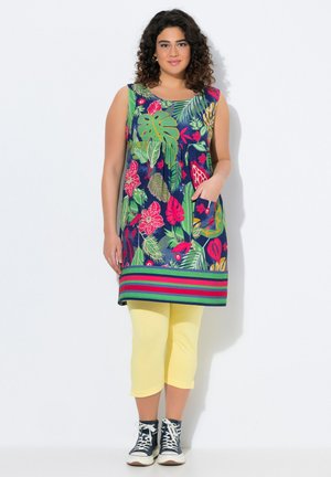 Floral tuniek in marineblauw met groene en roze patronen, met een ronde hals, mouwloos ontwerp en gestreepte zoom. Gepaarde met gele capri leggings.