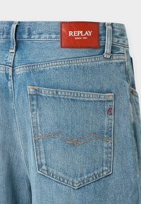 Τζιν παντελόνι από ντένιμ σε ανοιχτό μπλε χρώμα με καφέ δερμάτινο έμβλημα στη μέση με την επιγραφή "REPLAY". Διαθέτει πίσω τσέπη με κόκκινες ραφές.