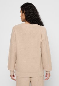 Beiger Strickpullover mit strukturiertem Muster, Rundhalsausschnitt und langen Ärmeln. Rippbündchen und -saum. Glatte Stoffoberfläche.