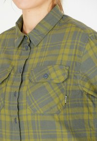Grön och gul rutig skjorta i flanelltyg med spetskrage, två bröstfickor och knäppning fram.