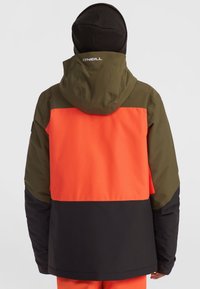 Veste de ski colorée avec capuche. Présente des panneaux orange, vert olive et noir. Fabriquée en matériau lisse et résistant à l'eau. Pas de marquages visibles.