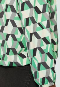 Gestructureerde stof met een geometrisch patroon in groen, zwart, grijs en lichtroze, met een losse pasvorm en gathered cuff detail.