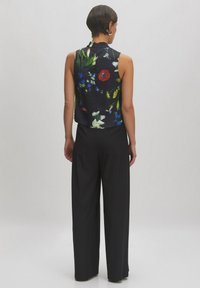 Mouwloze bloemenblouse met een zwarte achtergrond, versierd met levendige rode, blauwe en groene bloemen; gecombineerd met een wijde zwarte broek.