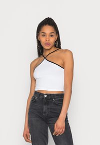 Top cropped branco com acabamento preto, apresentando um design de halter neck. Usado com jeans escuros de cintura alta. Tecido suave e estilo ajustado.