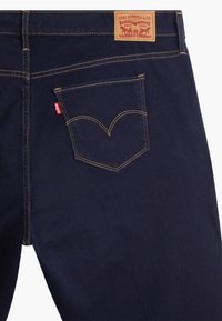 Mörkblå denimjeans med orange sömnad, med en bakficka med en böjd söm och en läderetikett som visar varumärket.