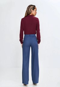 Burgundowa bluzka z długim rękawem i kołnierzykiem zestawiona z niebieskimi spodniami o wysokim stanie i szerokich nogawkach; gładka tkanina i dopasowany krój widoczne.