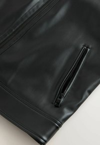 Veste en cuir noir avec une texture lisse, dotée de fermetures éclair proéminentes et d'un design structuré. Accentuée par une poche en biais.