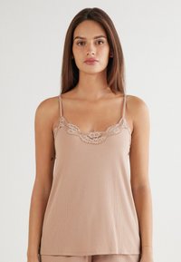Beige ribben tanktop met verstelbare bandjes, een kanten rand bij de hals en een ontspannen silhouet. Zachte textuur met subtiele details.