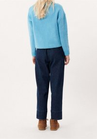 Ljust blå, fluffig tröja med långa ärmar, parat med mörkblå, löst sittande jeans som är upprullade vid anklarna, och bruna ankelstövlar.