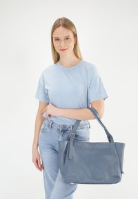Blaue strukturierte Lederhandtasche mit einem einzelnen Schulterriemen und goldfarbenen Beschlägen, vor einem neutralen Hintergrund präsentiert.