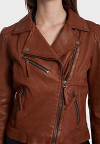 Braune Leder-Motorradjacke mit taillierter Passform, ausgestattet mit Reißverschlüssen, Druckknöpfen und zwei Seitentaschen. Eine gebrauchte Textur ist sichtbar.