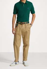 Grön polo skjorta, beige veckade byxor, flerfärgad randig bälte och vita sneakers med marinblå accenter. Klassisk avslappnad outfit.