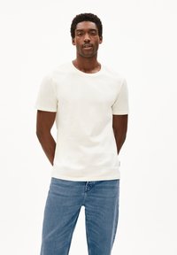 Katoenen, korte mouwen, ronde hals t-shirt in lichtbeige, gecombineerd met blauwe spijkerbroeken. Het t-shirt heeft een gladde textuur en geen patronen.