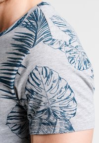 Grå kortærmet skjorte med et blåt tropisk bladprint på skulderen, fremhævende et blødt stof og design med rund hals.