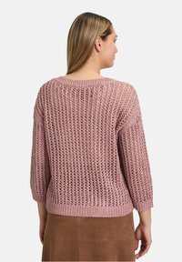 Różowy sweter dziany z otwartym splotem, z rękawami do łokcia i żeberkowym dekoltem oraz dołem. Nosi się go z brązową zamszową spódnicą.