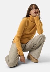 Maglione a collo alto color giallo senape in morbidissimo knit, abbinato a pantaloni a gamba larga in grigio chiaro con texture, e stivali platform chunky beige.