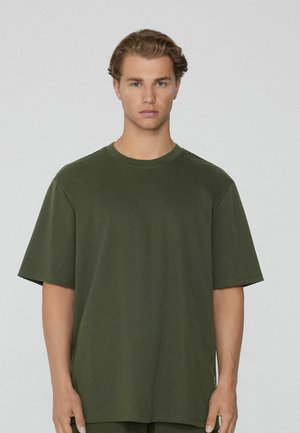 Camiseta de manga corta de color verde oliva, con cuello redondo, fabricada en suave algodón, que presenta un corte relajado y recto con detalles de costura mínimos.