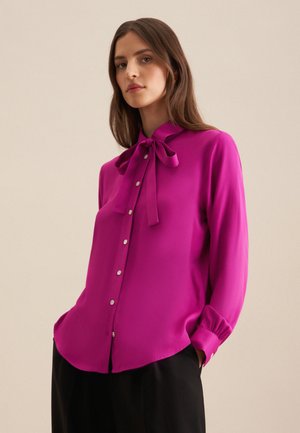 Fuchsia blouse met een strik rond de hals, lange mouwen, knoopsluiting aan de voorkant, zachte textuur en een licht gebogen zoom.