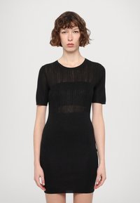 Svart tettsittende kjole laget av ribbestrikket stoff med korte ermer og rund halsringning; har en gjennomsiktig horisontal stripe over torsoen.