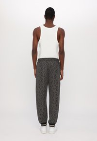 Černé jogger kalhoty s geometrickým vzorem, elastickým pasem a manžetami, spárované s bílým tílkem a bílými teniskami.