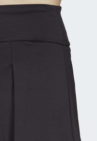 Sort atletisk skort med bred taljehæk, glat tekstur, plisseret design ved kanten og forstærket syning langs sømmene.