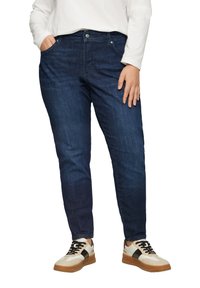 Ciemnoniebieskie dżinsy o prostym kroju, z przednimi kieszeniami i zapięciem na guzik. Noszone z białą koszulą z długim rękawem i trampkami.