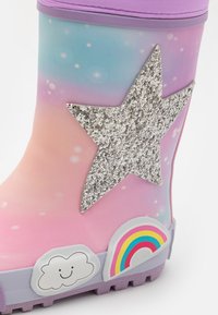 Botte de pluie en caoutchouc dégradé rose et bleu avec une grande étoile en paillettes argentées et des accents de nuage colorés et d'arc-en-ciel sur le côté. Semelle texturée.