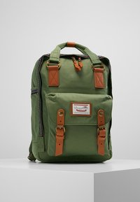 Zelený látkový batoh s hnědými akcenty, dvěma předními kapsami, nastavitelnými popruhy, horním uchopovacím držadlem a označením značky. Obsahuje zipové uzávěry.