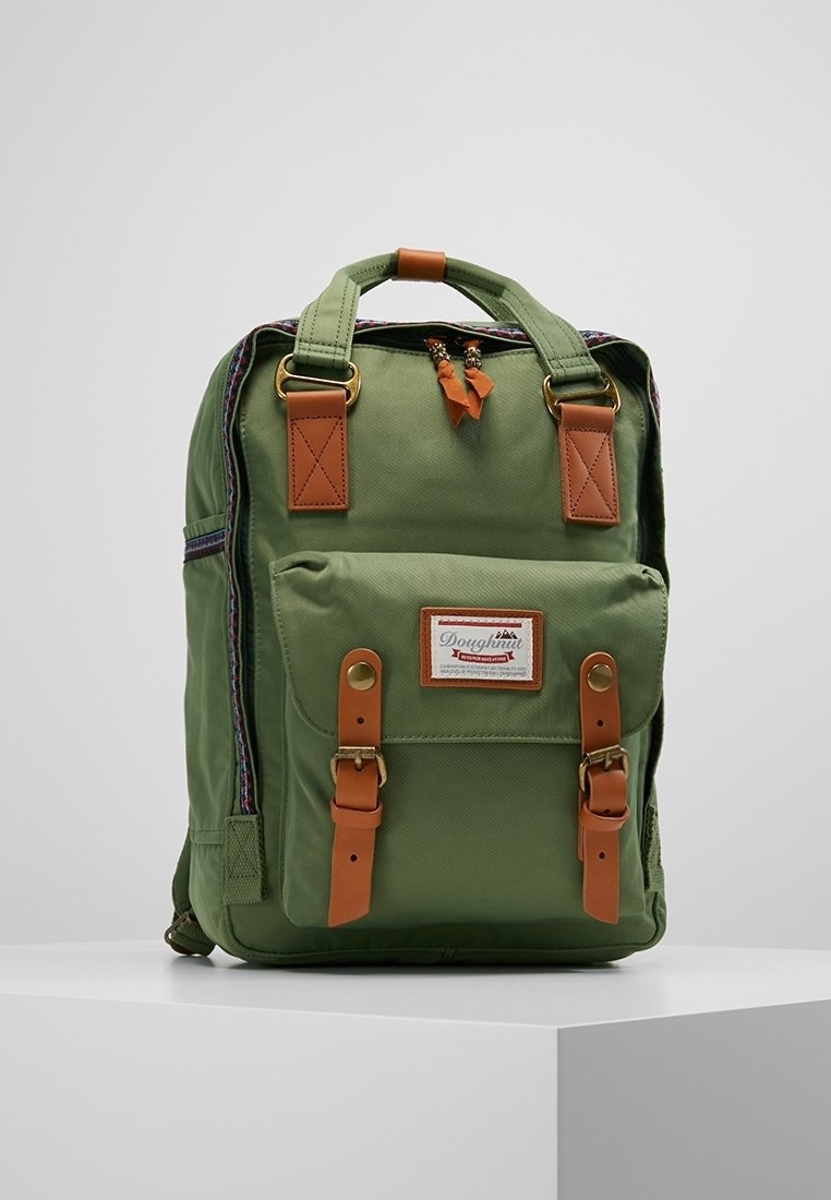 Zelený látkový batoh s hnědými akcenty, dvěma předními kapsami, nastavitelnými popruhy, horním uchopovacím držadlem a označením značky. Obsahuje zipové uzávěry.