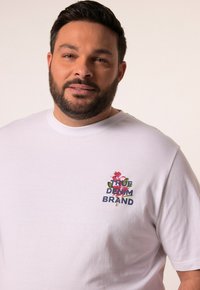 Bílá bavlněná tričko s barevným květinovým logem "True Denim Brand" na levé části hrudi. Krátké rukávy a klasický střih.