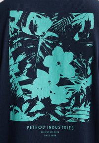 T-shirt bleu marine avec un motif floral et de feuilles turquoise. L'imprimé comprend diverses feuilles tropicales et fleurs avec une texture mate.