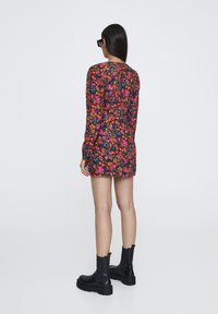 Vestido floral de manga larga, con fondo negro decorado con vibrantes flores rojas, rosas y naranjas, combinado con botas negras hasta el tobillo.