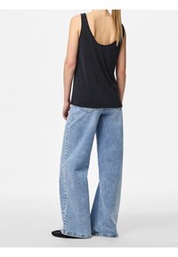 Svart linne med låg rygg, matchat med ljusblå vida jeans. Tyget verkar mjukt, med en avslappnad passform och minimal detaljering.