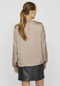 Lys beige silke bluse med smocket krave og manchetter, der har en nøglehulslukning bagpå. Sammen med en sort læder mini nederdel.