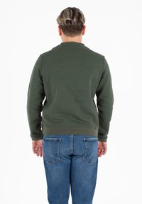 Donkergroene sweatshirt met lange mouwen en geribbelde boorden, gecombineerd met blauwe denim jeans. Heeft een gladde textuur en een elastische zoom.